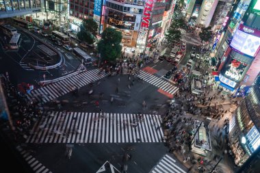 Yükselen manzara, Tokyo 'da Shibuya Geçidi' ni gösteriyor. Kalabalık çapraz kırlangıçlar üzerinden akıyor. Shibuya İstasyonu yakınlarında parlak reklam panoları, otobüsler ve taksiler hareket ediyor..