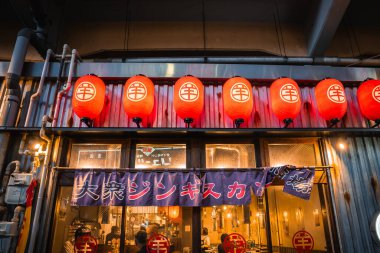 Tokyo izakaya mağazası önü kırmızı çene fenerleri, jingisukan noren, kıvrımlı metal cephe, görünür borular ve içerideki lokantalar ile parıldıyor..