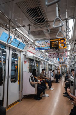 Gezginler Tokyo metro vagonunda yan yana oturuyorlar, bazıları telefonlarda, bazıları da pencereden dışarı bakıyor. Japonya 'da genel reklam ve elektronik ekran çizgisi ayrıntıları.