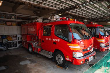 Kırmızı bir Hiroşima itfaiye aracı, ikinci bir kamyonla istasyon koyunda duruyor. Takside raflar, kanji, tavan lambaları ve yan hortumlar, yakın mesafeden görülüyor..