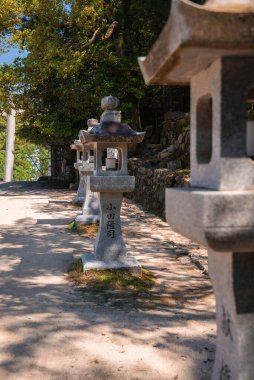 Japonya 'nın Hiroşima yakınlarındaki Miyajima' da Itsukushima Tapınağı kompleksine doğru yol gösteren yosunlu bir duvarın yanında oyulmuş kanji çizgisi olan geleneksel taş fenerler..