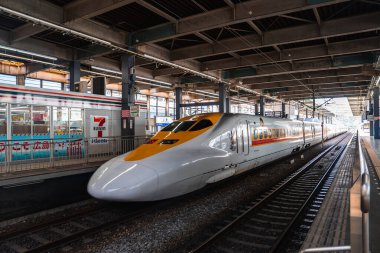 Beyaz ve turuncu Shinkansen Osaka, Japonya 'da kapalı bir platformda bekliyor. İstasyon tabelaları, otomatlar ve 7 Eleven büfesi gün ışığında yakınlarda oturuyorlar..