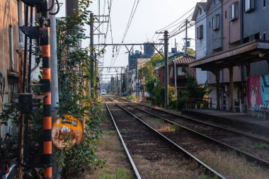 Osaka, Japonya 'da alçak katlı evlerin yanından geçen ikiz raylar mütevazı bir platform, dışbükey ayna, çizgili bir geçiş direği ve sıcak öğleden sonra ışığı altında kanatlar.