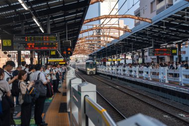 JR treni Osaka 'da bir Japon istasyonuna yakındır. Ofis banliyöleri çelik gölgeliklerin altında kuyruk, kanji tabelaları parlıyor, paslı kiriş köprüsü öğleden sonra aydınlığında rayları geriyor.