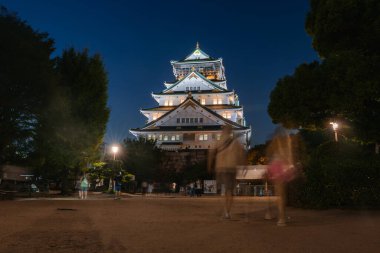 Osaka, Japonya 'daki Osaka Şatosu ziyaretçiler karanlıkta yürürken alacakaranlıktan sonra aydınlanıyor. Ilık lamba ve ağaçlar tarihi kaleyi altın süslemelerle donattılar..