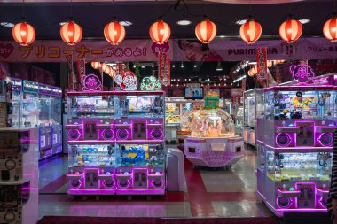 Osaka 'da parlak ışıklandırılmış bir atari salonunda peluş oyuncaklarla dolu sıra sıra pençe makineleri görülüyor. Neon pembe ve mor ışıklar cama yansıyor, kırmızı fenerler asılıyor ve Japonca işaretler parlıyor..