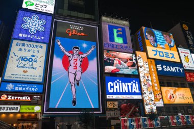 Dotonbori, Osaka, Japonya 'da Çinli ve Vaat reklamlarıyla çevrili Glico' nun koşu tabelaları. Dikey neon paneller, karanlık ışıktan sonra çıtır çıtır parlar..