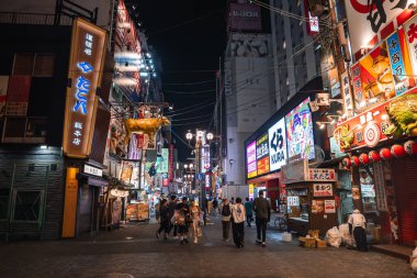 Yayalar Osaka 'daki Dotonbori boyunca ilerlerler, neon ışıklarının altında, altın kirpi balığı feneri, ve Kura suşi işareti, gıda tezgahları ve dükkan önleri parlar..