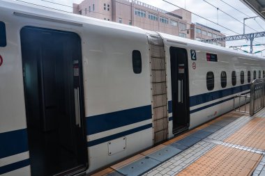 Mavi çizgili beyaz bir Shinkansen Osaka istasyonunda duruyor. İkinci vagonda, tentenin altındaki kapılar aerodinamik vücut ve gün ışığında düzenli işaretler gösteriyor..