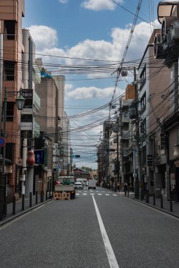 Sessiz bir Kyoto caddesi, içinde fenerler, işaretler ve elektrik kabloları olan yükselen binaların ortasından geçer. Yumuşak gün ışığı, dağınık bulutlar, kalın bulutlar ve tek bir merkez çizgi boş yola rehberlik eder..