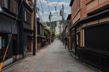 Kyoto Gion veya Higashiyama 'daki dar bir taş şeritte Machiya, kırmızı fenerler, bambu aksanları, bisikletler, elektrik hatları ve yayalar olmadan alçak saçaklar görülüyor..
