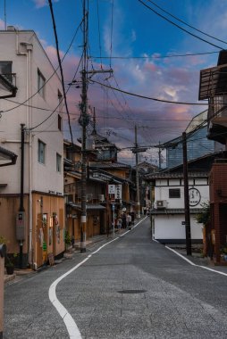 Machiya binaları, kanji işaretleri, fenerler ve alacakaranlıkta saksı bitkileri, birkaç yayalar, birleşik çizgiler ve desenli taş döşeme ile yavaşça kıvrımlı bir Kyoto caddesi..