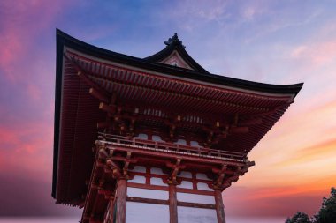 Alacakaranlıkta Kyoto 'daki kırmızı ahşap tapınak kapısının alçak açılı görüntüsü günbatımı renklerinin tarihi tapınak girişini çerçeveledikçe pagoda saçağları ve kereste doğramacılığı göze çarpıyor..