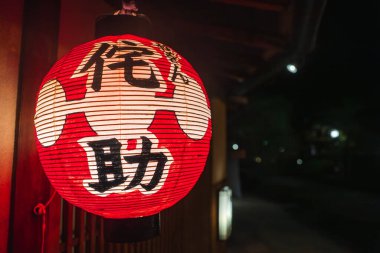 Siyah beyaz kanjili kırmızı bir kağıt fener gece Kyoto 'daki ahşap bir mağazada asılı, sığ alan derinliği ve yumuşak bokeh ışıkları ile yakın çekim.