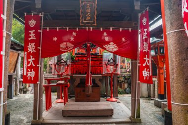 Japonya 'nın Kyoto kentindeki Fushimi Inari Taisha' da kırmızı bayrakları ve tilki motifleriyle küçük bir Shinto sunağı duruyor. Yumuşak gün ışığı fenerleri, ipleri, tabureleri ve bir adak masasını gösterir..