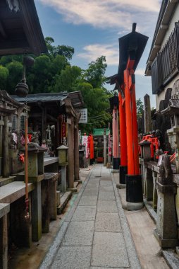 Granit fenerler, kırmızı önlüklü tilki heykelleri ve minyatür torii Japonya 'nın Kyoto kentindeki Fushimi Inari Taisha' nın arkasında bambu olan taş bir patika çiziyor..