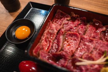 Yakından bakınca, Japonya 'nın Nara kentinde çiğ yumurta sarısı soslu lavantalı bir bentoda az pişmiş et görünüyor. Ilık iç ışık ve sığ alan derinliği zengin dokuları vurgular.