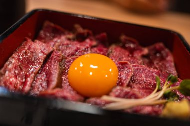 Yakından bakınca Japonya, Nara 'da kurutulmuş sığır eti dilimleri ve çiğ yumurta sarısı, yanında mikroçimler, sıcak bir ev ışığı ve sığ bir alan derinliği görünüyor..