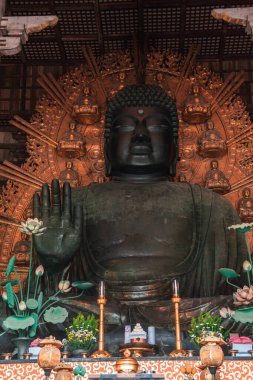 Nara 'daki Todai ji' nin bronz Buda heykeli altın mandorla 'nın önünde oturur, sağ el kaldırılır, nilüfer ve tütsü tabanda, sıcak iç ışık metal ve ahşabı ortaya çıkarır.