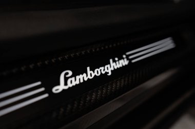 Aydınlatılmış Lamborghini metninin her iki tarafında üç şerit, parlak siyah ve karbon fiber doku, profesyonel bir oto atölyesinde kapalı, yumuşak yönlü ışık