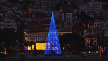 Funchal, Madeira 'nın hava alacakaranlık manzarası, liman gezinti güvertesi, aydınlık şehir merkezi, konik Noel ağacı kırmızı ve mavi bisiklet, neoklasik cephe ve tepe kenarındaki evler..
