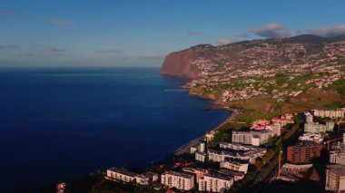 Hava aracı taramasına göre Funchal, Madeira, Portekiz sahillerinde oteller, evler, çakıl plajları, rıhtımlar, teraslı tepeler, beyaz evler ve kırmızı Cabo Girao kayalıkları altın saatinde..