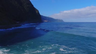 Hava görüntüsü volkanik kayalıkları, turkuaz suları, bir kıyı köyünü ve Funchal, Portekiz yakınlarındaki üs boyunca düz bir günışığında pürüzsüz bir hareketle dar bir yolu gösteriyor..