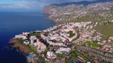 Hava görüntülerine göre Funchal, Madeira sahilleri beyaz bloklar, kırmızı çatılar, muz terasları, sahil havuzları, rıhtımlar, pas rengi uçurumlar, tekne kalkışı, vinçler ve parlak ışıklı villalar..