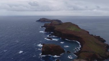 Hava görüntüsü Ponta de Sao Lourenco, Madeira, Portekiz 'deki kırmızı kahverengi kayalıkları ve deniz yığınlarını gösteriyor. Atlantik dalgaları, hafif bulutlu ışık, yavaş ilerleyen hareket