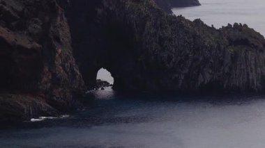 Hava aracı geçidi Portekiz 'in Madeira adasındaki karanlık bazalt kayalıklarında bir deniz kemeri gösteriyor. Yumuşak dalgalar koyu mavi suyun üzerinde serin ışık kayarken koyda tur atar..