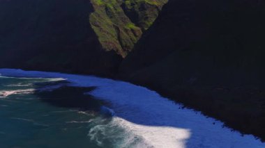 Portekiz 'deki Madeira uçurumlarının havadan görünüşü, Atlantik dalgaları, beyaz sörf şeritleri, düşük güneş, yavaş pan gibi dar kayalık bir kıyı üzerindeki V çentikleri ve yeşil teraslar