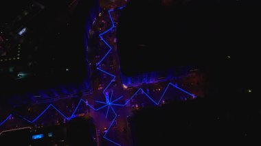 İnsansız hava aracı bir Funchal, Madeira kavşağı üzerinde döner ve döner. Mavi LED zigzag çizgileri tarafından aydınlatılır. Daireleri, park edilmiş arabaları ve küçük ışıklı havuzu olan bir yıldız deseni oluşturur..