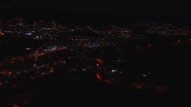 Gece hava göstergeleri Madeira, Funchal kenar mahalleleri ve yamaçtaki yolları gösteriyor. Sıcak sodyum ışıkları, daha parlak bir şehir merkeziyle dolambaçlı yolları ve ev kümelerini takip eder..