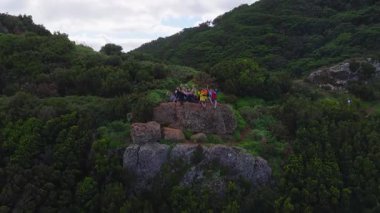 Hava aracı Portekiz, Madeira 'da yıpranmış bir kaya üzerinde sallanan yürüyüşçülerden geri çekiliyor. Sarp yamaçlar ve volkanik oluşumlar grubu sarar..