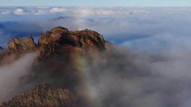 Madeira, Portekiz 'deki Pico do Arieiro sırtı üzerinde. Sis girdabında kayalık kayalıklar yükselir, sisli bir yay belirir ve ılık, düşük ışık dokuyu otlatır..