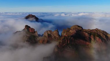 Sabahın erken saatlerinde Madeira Pico do Arieiro, Portekiz 'deki bazalt kayalıklarda uzun gölgeler oluşur. Hareketli bulut kümeleri yeni zirveler ve sönük bir sis halkası ortaya çıkarır..