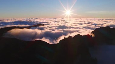 Pico do Arieiro, Madeira, Portekiz 'de bulutların tepesindeki hava aracı. Tepelerden sis akar, zirveye yakın radar kubbesi, güneş ışığı ve mercek parlaması görünür..