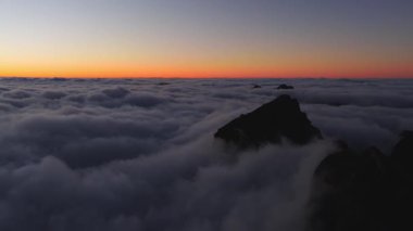 Hava görüntüsü Portekiz 'in Madeira şehrinde bulutların üzerinde volkanik Pico do Arieiro hareketini gösteriyor. Kamera gölgeli zirvelerin ve pastel ışığın altındaki uzak adaların yanından süzülüyor..