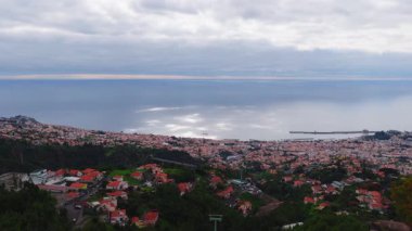 Portekiz, Madeira Adası, Funchal 'ın havadan görünüşü, dik yamaçlarda terracotta çatıları, körfez ve dalgakıran, teleferik direkleri, yemyeşil ağaçlar ve küçük bir yelkenli teknesi..