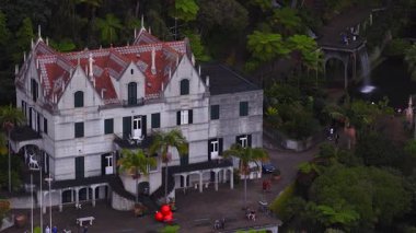 Hava manzarası Monte Sarayı 'ndaki konakları, terasları, kemerli şelaleleri, göleti, ziyaretçileri, kırmızı eğreltiotlarını, Monte, Funchal, Madeira' daki eğreltiotlarını gösteriyor..