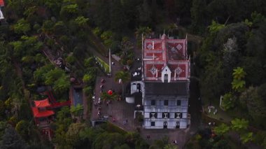 Hava görüntüsü, kırmızı ve beyaz kiremitli çatı ve taş teraslı Monte Palace villası, kırmızı pagoda, köprü, gölet ve öğleden sonra aydınlığında ziyaretçileri olan Tropikal Bahçesi gösteriyor..