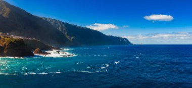 Yüksek volkanik kayalıklar, Ponta de Sao Lourenco yakınlarında veya Sao Vicente 'nin doğusunda, Madeira' nın kuzey kıyısında beyaz sörf, berrak ışık ve çok az bulut ile Atlantik 'le buluşur..