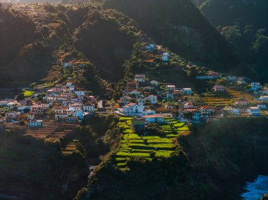 Hava manzarası teraslı tarlalar, beyaz evler ve Portekiz 'in Madeira kentindeki dik kayalıklarda küçük bir kilise gösteriyor.