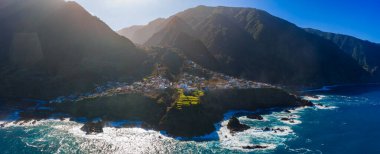 Hava panoramik görüntüsü Portekiz 'in Madeira Adası' nda volkanik kayalıklar ve Atlantik arasında, terasları, koyları ve öğleden sonra ışığı olan küçük bir kıyı köyü gösteriyor..