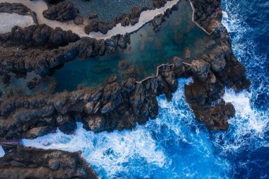 Porto Moniz, Madeira, Portekiz 'deki Atlantik' in yakınlarındaki volkanik kayalar zümrüt gelgit havuzlarını kaplar. Adımlar ve duvarlar, yumuşak geç ışığın dokuyu ortaya çıkarması gibi erişime rehberlik eder.
