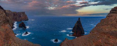 Portekiz 'in Madeira bölgesindeki Ponta de Sao Lourenco' da, koyu mavi Atlantik üzerinde kızıl kahverengi kayalıklar ve sivri deniz yığınları yükselir. Yumuşak pastel ışık volkanik kayaları gün batımına yakın ısıtır.
