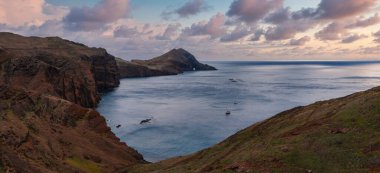 Portekiz 'in Madeira şehrinde engebeli, paslı kayalıklar, alacakaranlıkta geniş bir koy oluşturuyor. Küçük tekneler sakin Atlantik sularında dinleniyor. Panoramik manzara kaya yığınları ve kurak volkanik yamaçları gösteriyor..