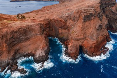 Hava görüntüsü Portekiz, Madeira 'daki Ponta de Sao Lourenco' da engebeli kırmızı kayalıklar ve bazalt kemerler gösteriyor. Gün ışığında tabanında köpük dalgaları ve canlı volkanik dokular..