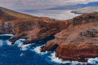 Ponta de Sao Lourenco, Madeira, Portekiz 'in hava manzarası, dalgalar toprak ve pas kaya raflarını vururken, yayılmış bulutlu ışıkta katmanlı lav ve sivri burunlar.