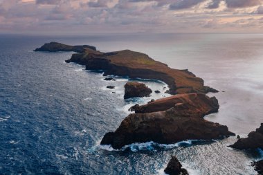 Hava manzarası Portekiz, Madeira 'daki Ponta de Sao Lourenco' da engebeli volkanik kayalıklar ve deniz yığınları gösteriyor. Bulutlu gün ışığı kayalara ve sörflere yumuşak tonlar atıyor..